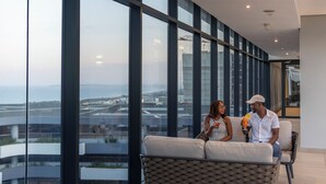 Habitación de hotel moderna con amplios ventanales de piso a techo, un sofá confortable y vistas a la ciudad y al aeropuerto.