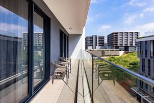 A balcony with a glass railing, outdoor seating, and a view of modern buildings.