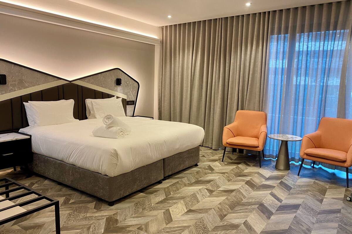 A hotel room with a large bed, two armchairs, a small table, and a herringbone-patterned floor.