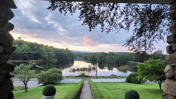Un arc en pierre encadre une vue sur un lac, un sentier et des haies soigneusement taillées.