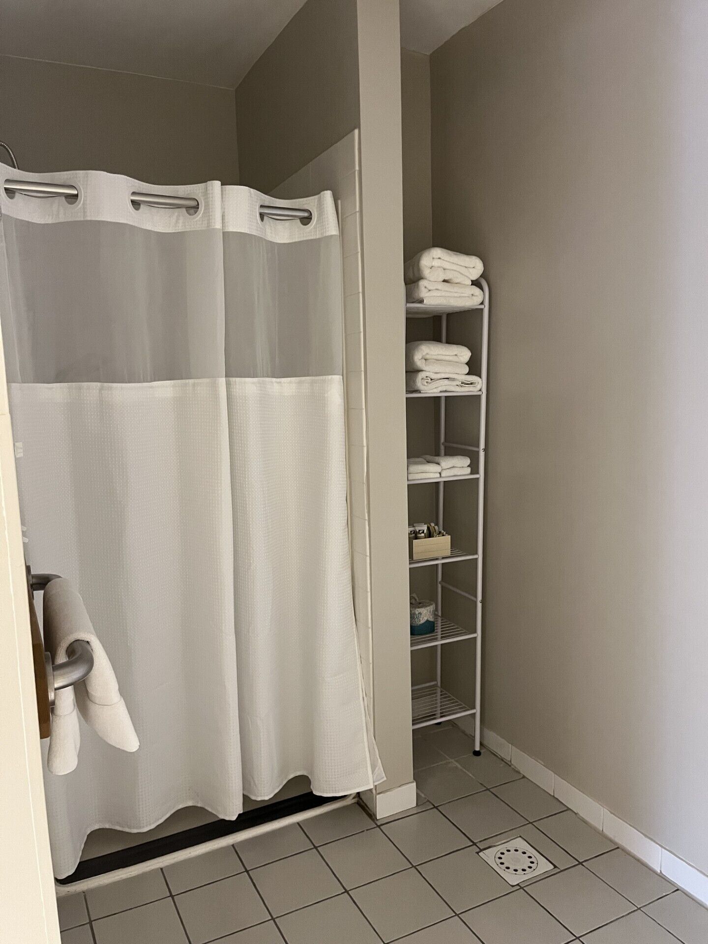 A bathroom with a shower curtain, a towel rack, and a shelf with folded towels.