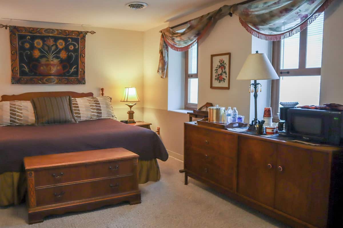 A bedroom with a bed, two bedside tables with lamps, a dresser, a television, and a window with curtains.