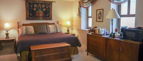 A bedroom with a bed, two bedside tables with lamps, a dresser, a television, and a window with curtains.