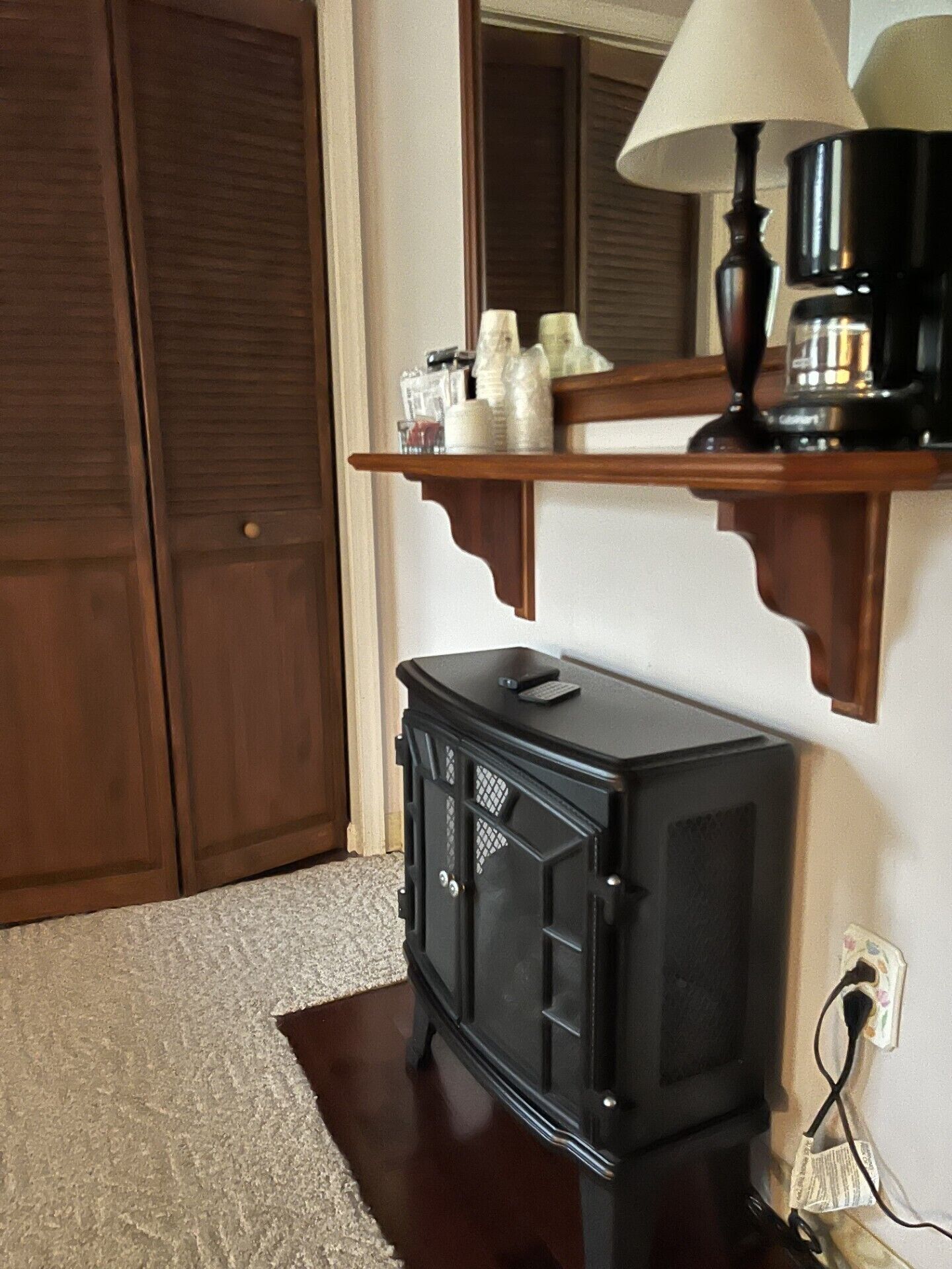 Une pièce avec une armoire en bois, un poêle noir, un miroir et une étagère où sont posées des bouteilles et des verres.