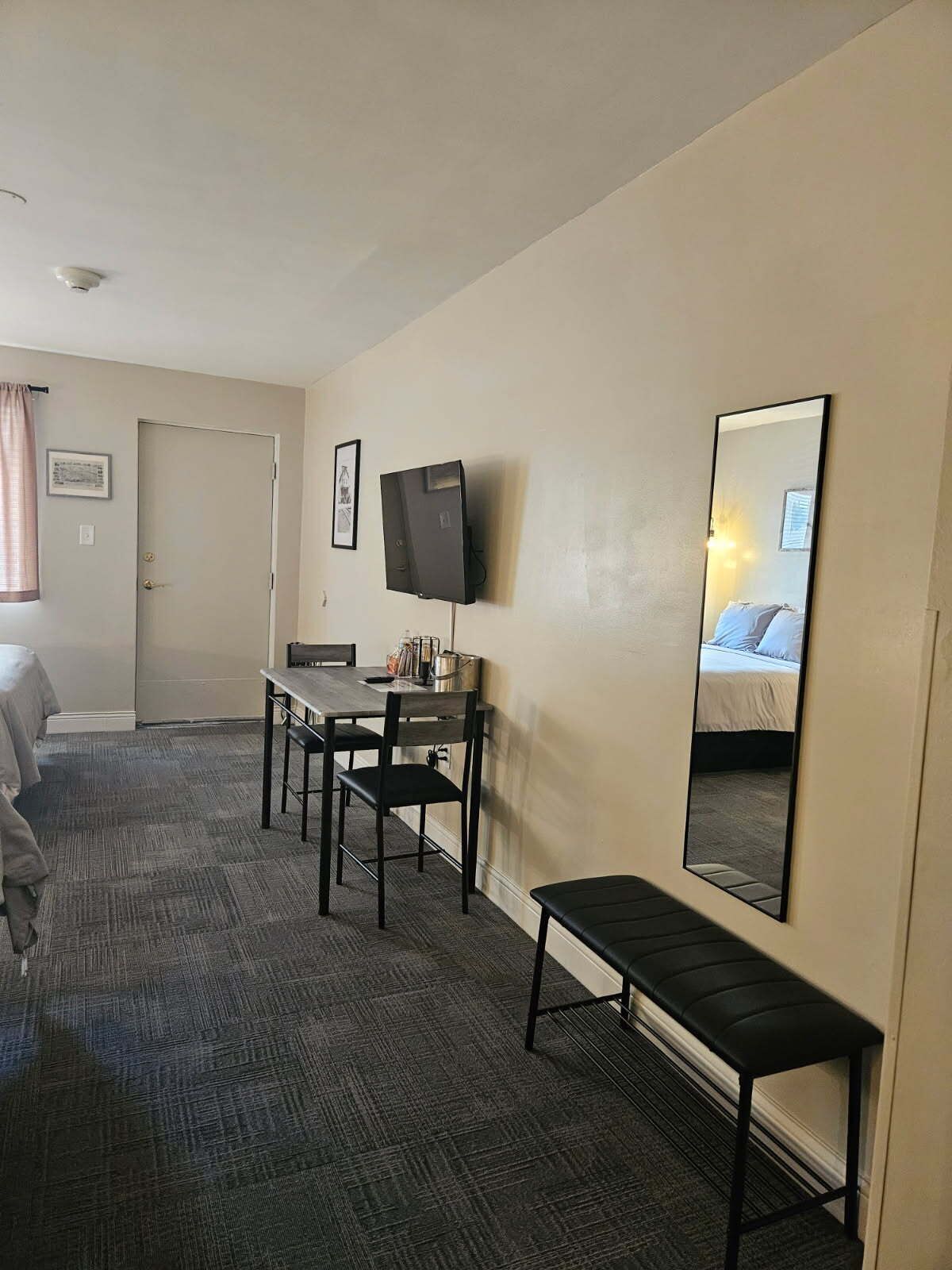 Una habitación de hotel con cama, escritorio con silla, televisión montada en la pared y un banco.