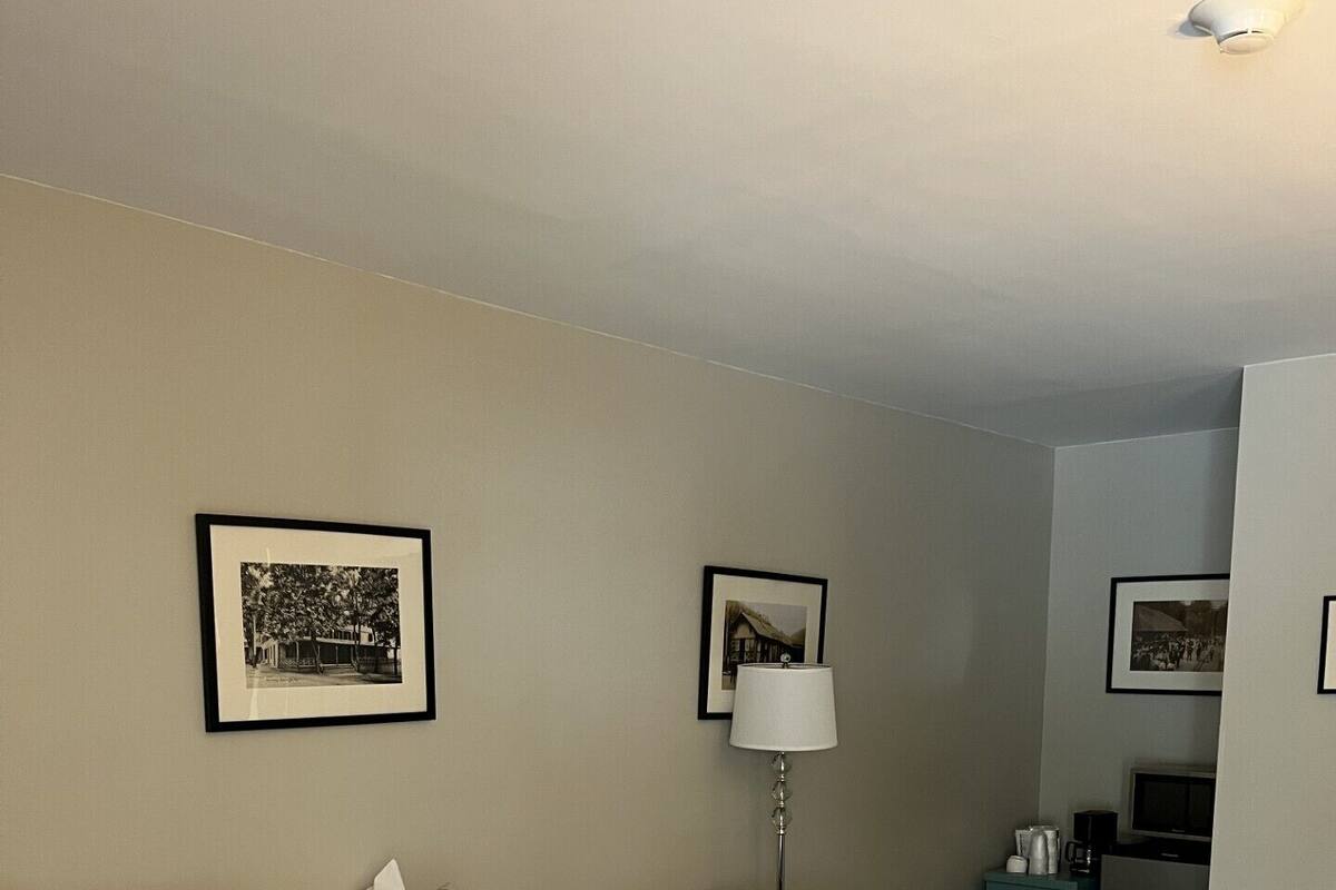 A hotel room with a large bed, a chair, a desk with a lamp, and framed pictures on the wall.