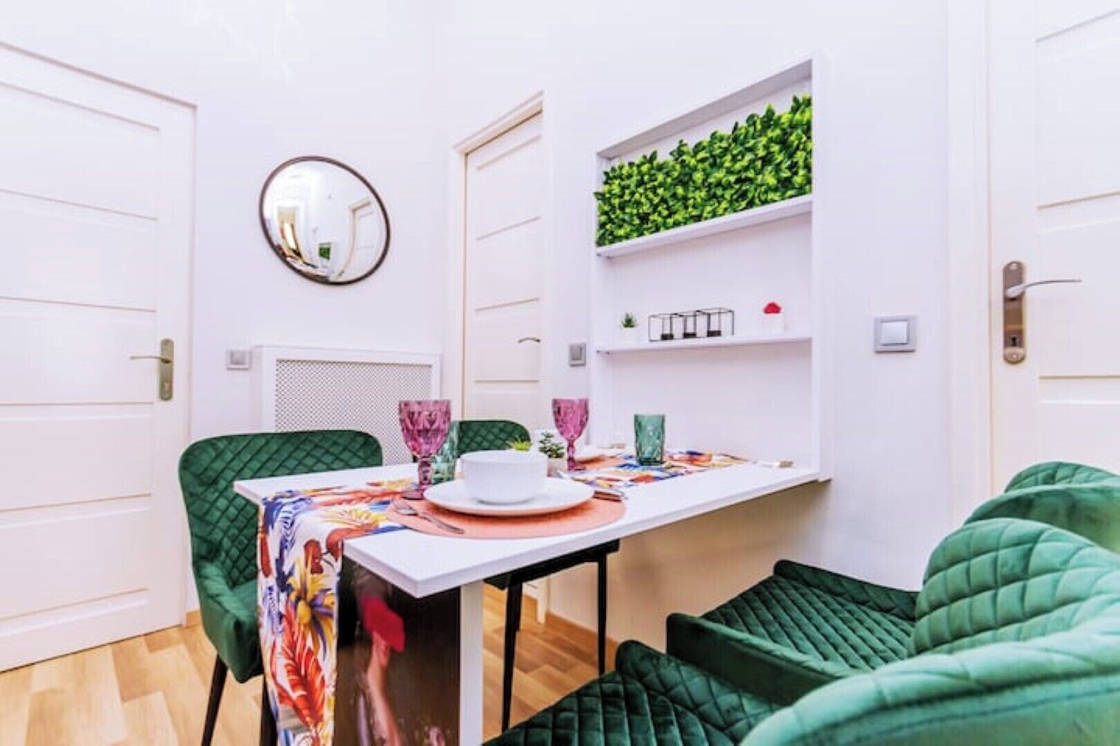 A compact room with a dining table, chairs, a mirror, and a green wall shelf.