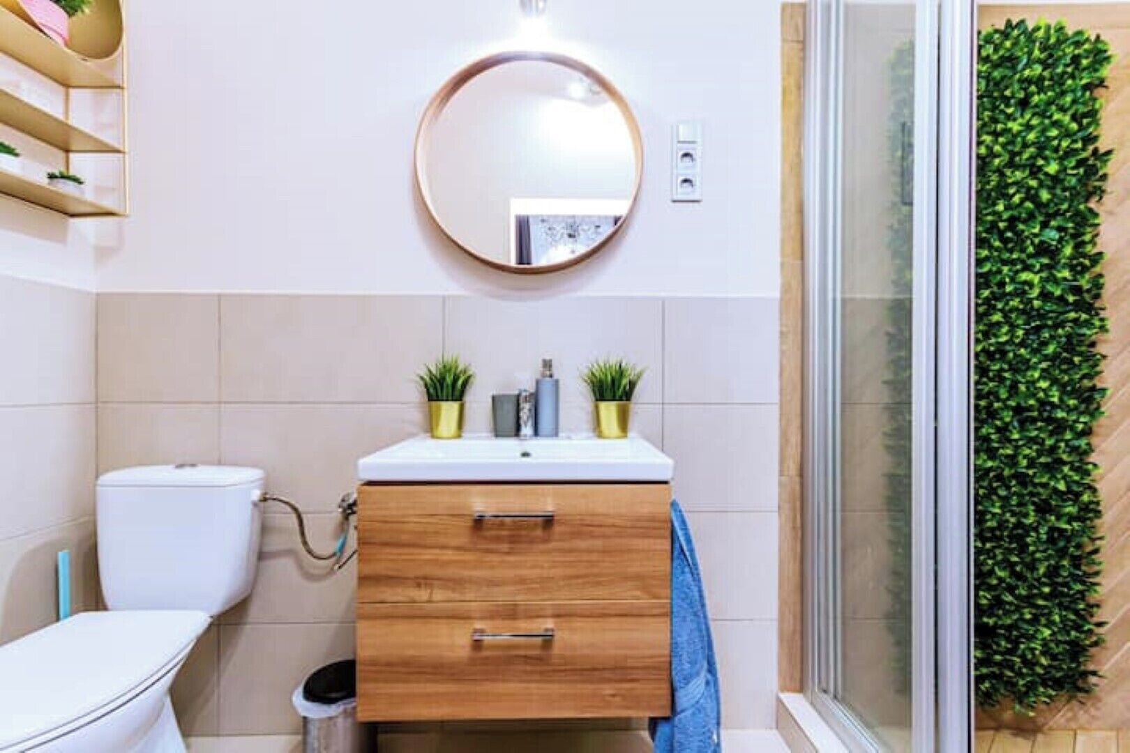 A bathroom with a toilet, a sink with two potted plants, a wooden cabinet, a mirror, and a green wall.