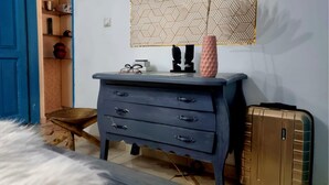 Una habitación con un aparador azul, una maleta y un papel tapiz estampado.