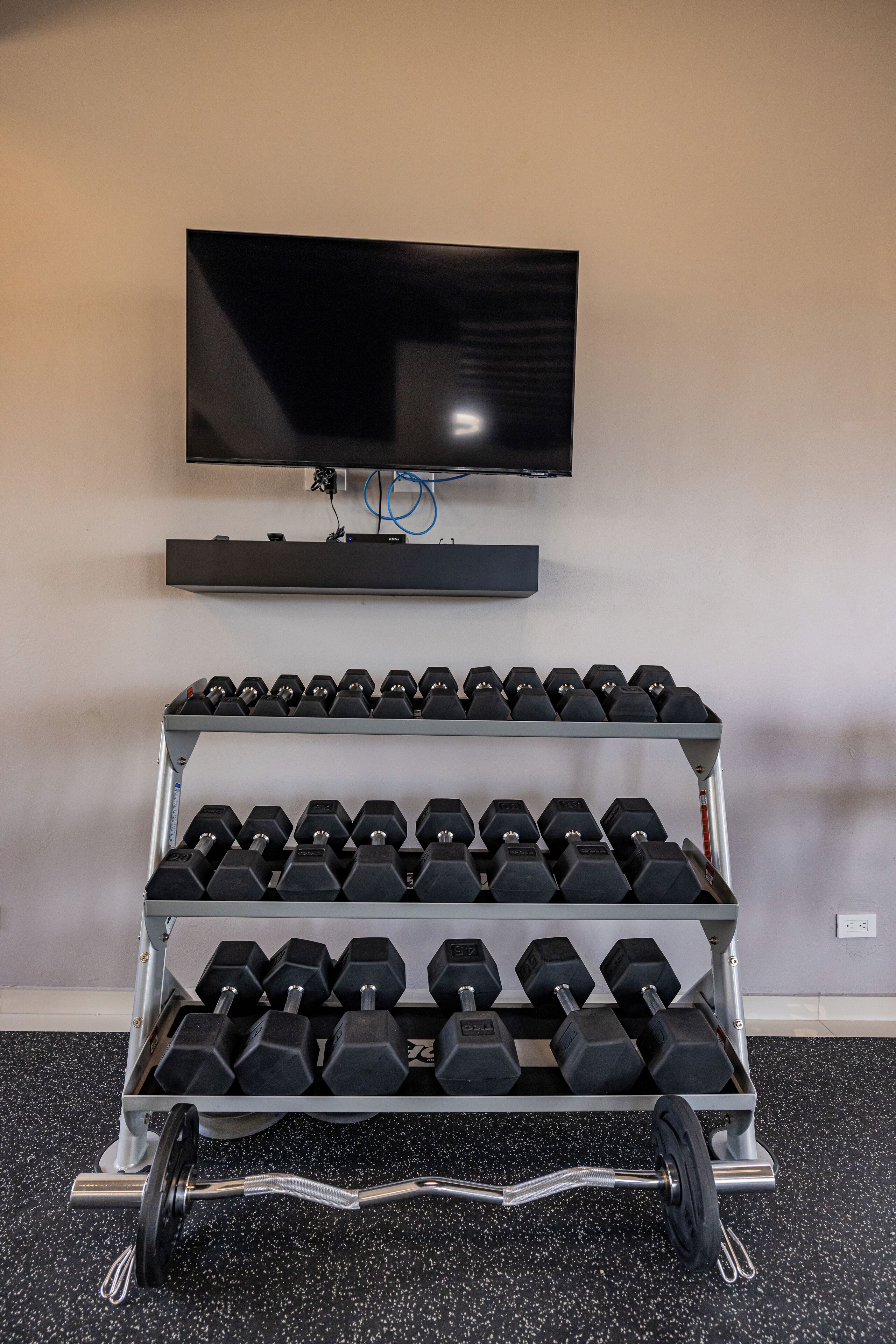 Une salle de sport à domicile avec un téléviseur fixé au mur, au-dessus d’un porte-haltères et d’une barre d’haltérophilie.