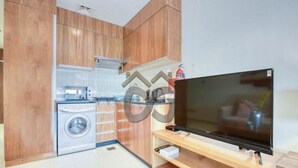 Eine kleine Küche mit Holzschränken, einer Waschmaschine und einem Flachbildfernseher auf einem Holzboden.