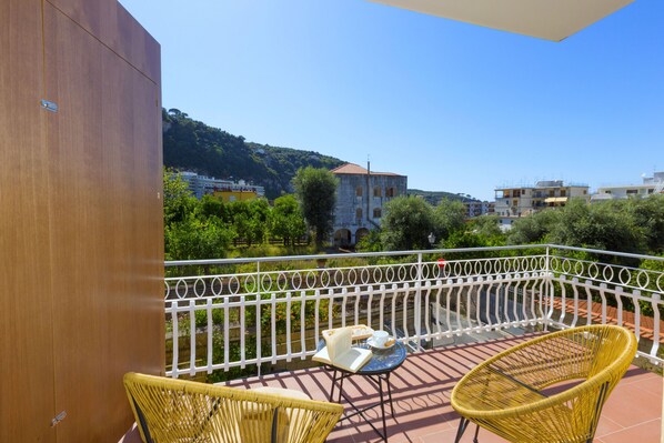 A balcony with wicker chairs and a table, overlooking a cityscape with buildings and greenery. - Estate4home - Suites 21 (Sorrento)
