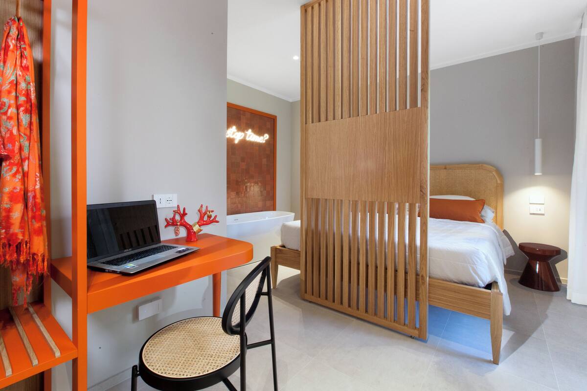 Ein modernes Hotelzimmer mit einem Holztisch, einem Laptop und einem Stuhl, einem Bett mit weißer Bettwäsche und einem Holzboden.