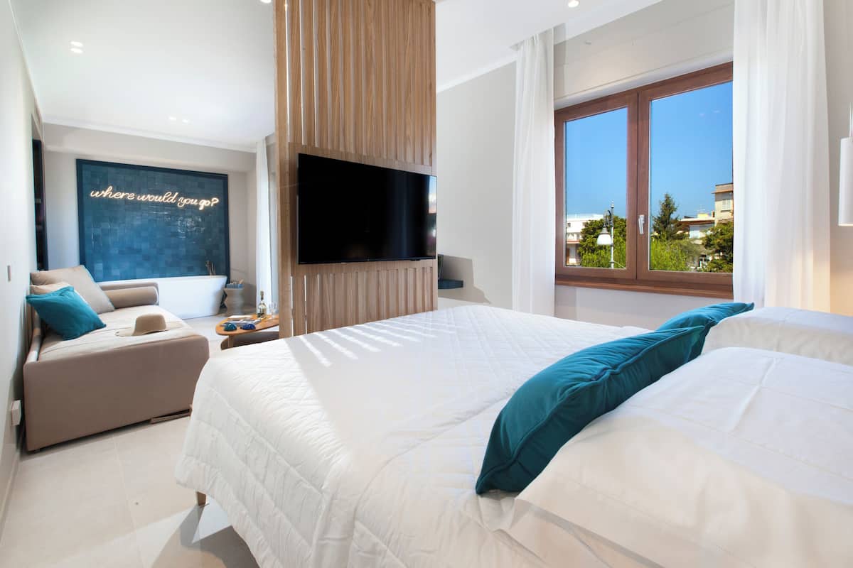 Ein modernes Schlafzimmer mit einem großen Bett, einer Couch, einem Flachbildfernseher und Blick ins Freie.