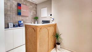 A reception area with a reception desk, a sign indicating 'Suites 21', a plant, and a wall-mounted light fixture. - Estate4home - Suites 21 (Sorrento)