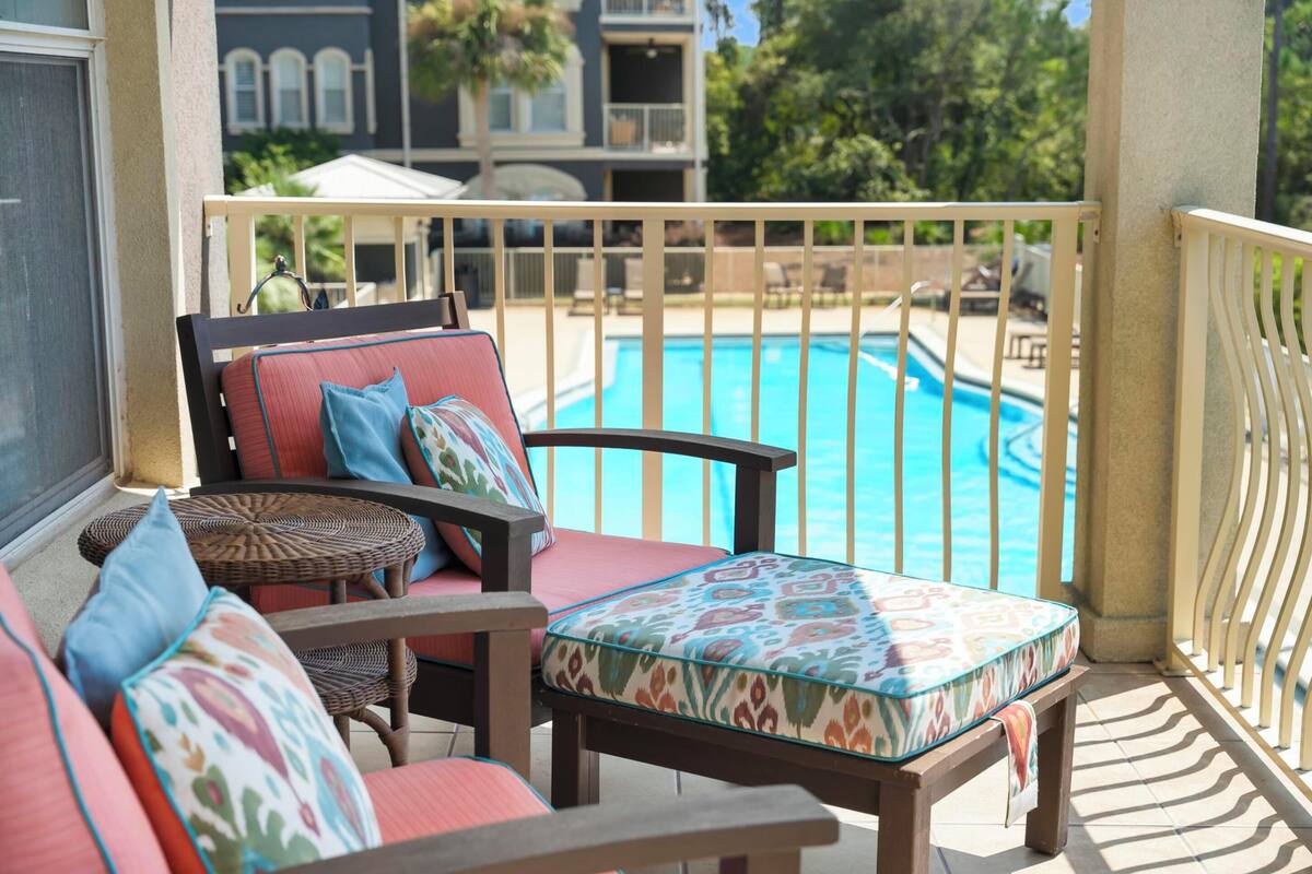A balcony with a pool view, wicker furniture, and a railing.