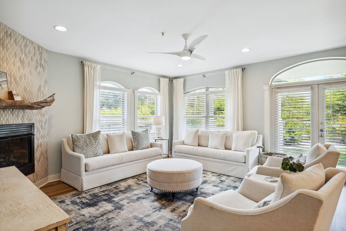 A spacious living room with a fireplace, two sofas, a round ottoman, and a ceiling fan.