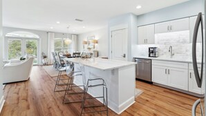 A modern kitchen with white cabinetry, a large island, and a dining area with bar stools. - Seaview Villas by Panhandle Getaways (Santa Rosa Beach)
