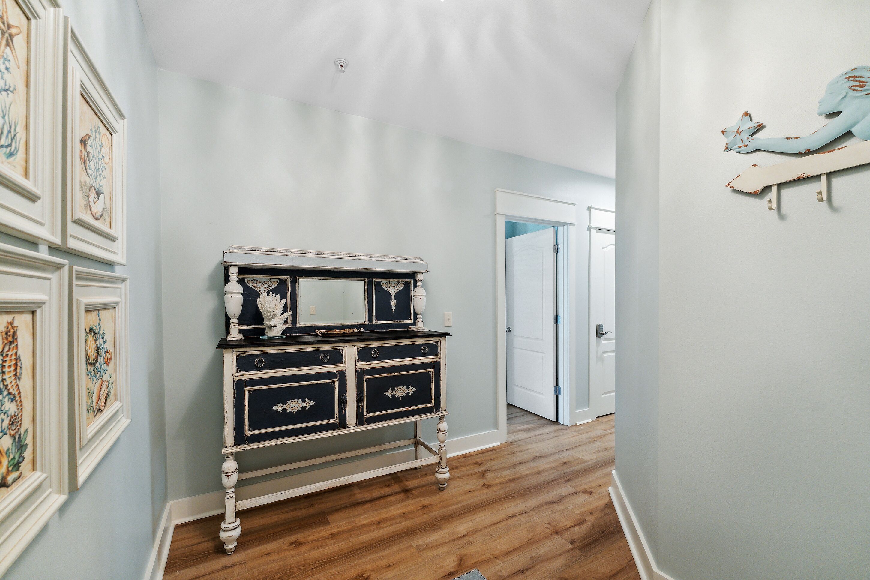 A hallway with a vintage-style dresser, framed artwork on the walls, and a wooden floor.