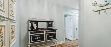 A hallway with a vintage-style dresser, framed artwork on the walls, and a wooden floor.