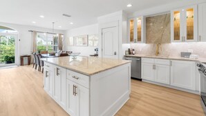 A modern kitchen with white cabinetry, a large island, and a view of greenery outside. - Seaview Villas by Panhandle Getaways (Santa Rosa Beach)