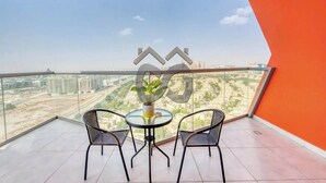 A balcony with a table and chairs, a potted plant, and a view of a cityscape. - Serene 2 Bedroom Apartment in Dubai Silicon Oasis (دبي)