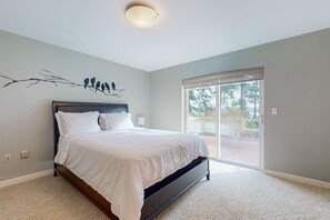 A bedroom with a large bed, a wall-mounted branch with birds, a window with a view of the outdoors, and a ceiling light. - Saratoga Passage waterview home with sunrise view, bbq and deck (Coupeville)