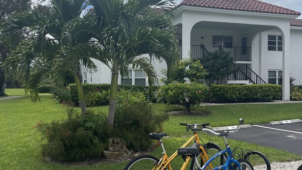 A white building with a red-tiled roof, a gravel pathway, and two bicycles parked on the side. - It is at the heart of Naples. Minutes from beach. Condo w/ pools, tennis, golf.  (Naples)