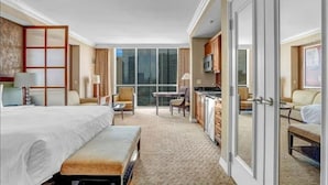 Una habitación de hotel con una cama grande, un escritorio, una silla, un sofá, un televisor y un ventanal corredero que da a un balcón.