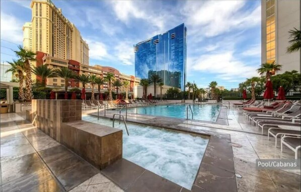 A hotel pool area with a hot tub, lounge chairs, and palm trees.