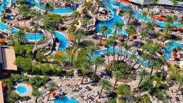 Vista aérea de un complejo turístico con varias piscinas, palmeras y tumbonas.