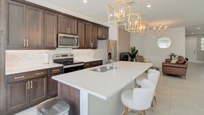 A modern kitchen with dark wood cabinets, a white countertop, stainless steel appliances, and a central island with bar stools. - Stunning Brand New 3 Bedroom, 2.5 Bathroom Luxury Townhome with Loft. (Deerfield Beach)