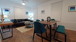 Un salon moderne avec un canapé foncé, une table basse ronde, des fauteuils turquoise et une table à manger en bois.