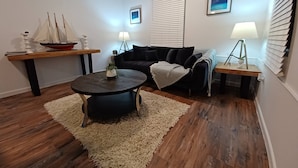 Un salon avec une table basse ronde de couleur sombre, un canapé noir, une table d’appoint en bois et une petite maquette de bateau.