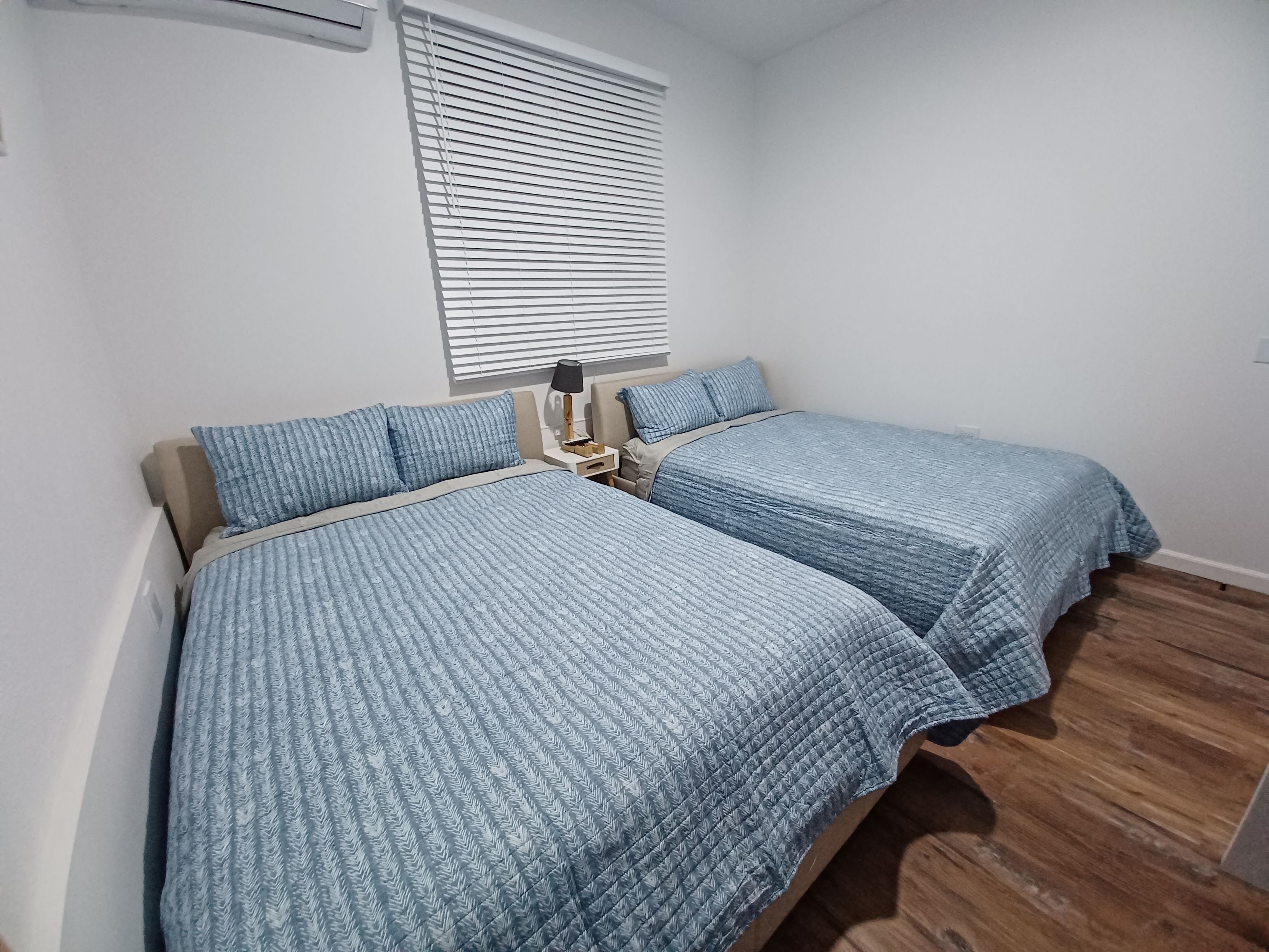 Un dormitorio con dos camas, una mesita de noche, una lámpara y una ventana con persianas.