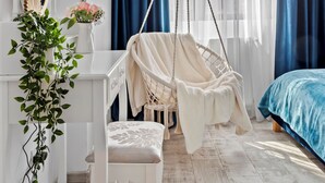 Ein Schlafzimmer mit Hängesessel, Schminktisch mit Spiegel und einem Bett mit blauer Bettwäsche.
