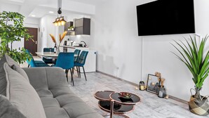 Ein modernes Wohnzimmer mit einem grauen Sofa, einem runden Couchtisch und einem Essbereich mit blauen Stühlen.