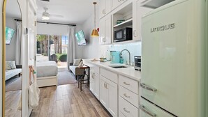 A modern kitchen with white cabinets, a unique refrigerator, a microwave, and a teal coffee maker.