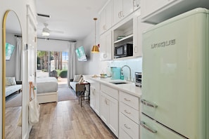 Una cocina moderna con armarios blancos, un refrigerador único, microondas y una cafetera color turquesa.