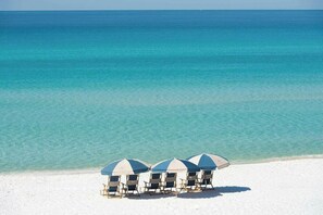 Una playa con tres sombrillas y cuatro sillas de playa.