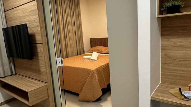 Une chambre d’hôtel moderne équipée d’un lit, d’un bureau, d’une chaise, d’une télévision et d’une petite plante.