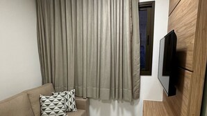 Un salon moderne avec un canapé beige, un téléviseur fixé sur un mur en bois et une fenêtre avec des rideaux.