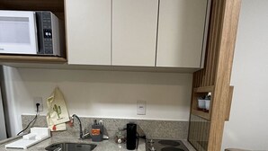 Une cuisine compacte équipée d’un four à micro-ondes, d’un évier et d’une cuisinière. On y trouve un petit plan de travail avec une machine à café et un cactus décoratif.