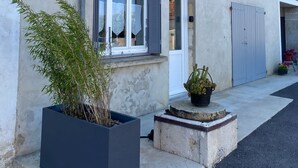 Een gebouw met een witte gevel, een deur en ramen. Er staan planten voor het gebouw.