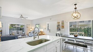 Une cuisine moderne dotée d’un grand îlot central, de meubles blancs et d’un ventilateur de plafond.