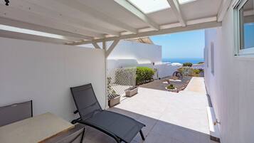 Un patio iluminado por el sol con una silla de descanso, una mesa y vistas al mar.