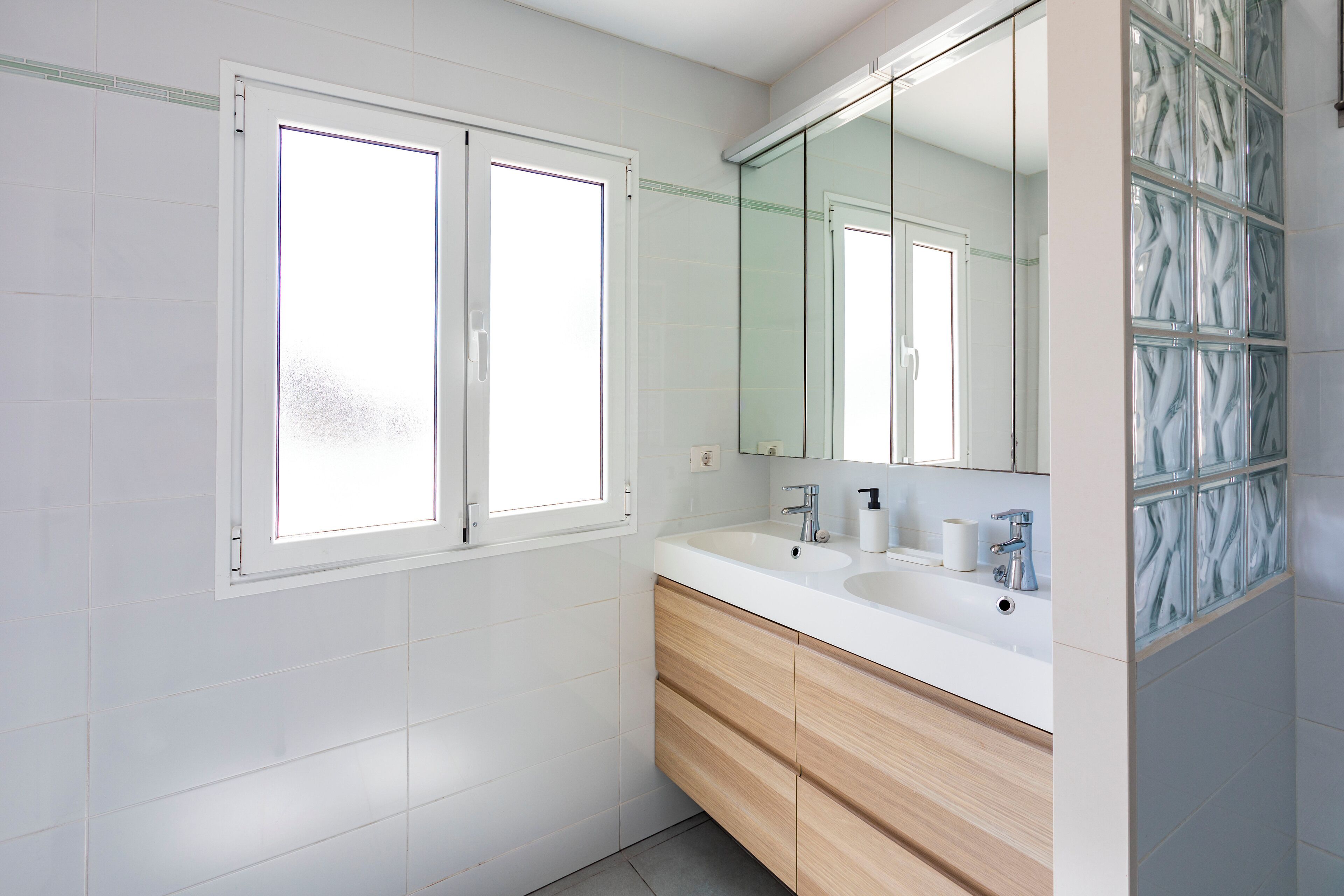 A modern bathroom with two sinks, a large mirror, and a window.