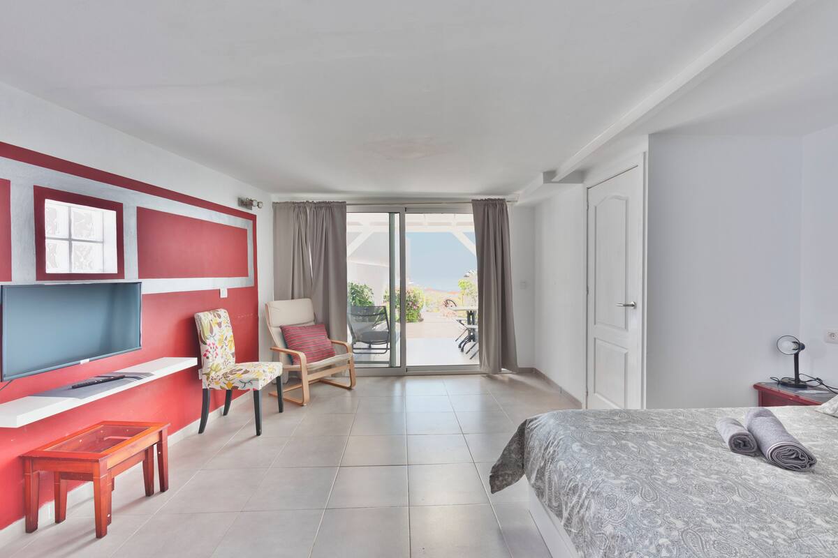 Quarto de hotel com cama, escrivaninha com cadeira, televisão e varanda com vista.