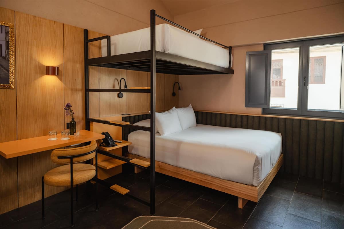 A bunk bed room with a desk, chair, and a window.