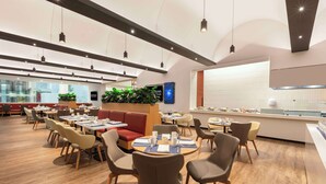 Un restaurante moderno con mesas redondas, asientos cómodos y un amplio ventanal con vistas a la ciudad.